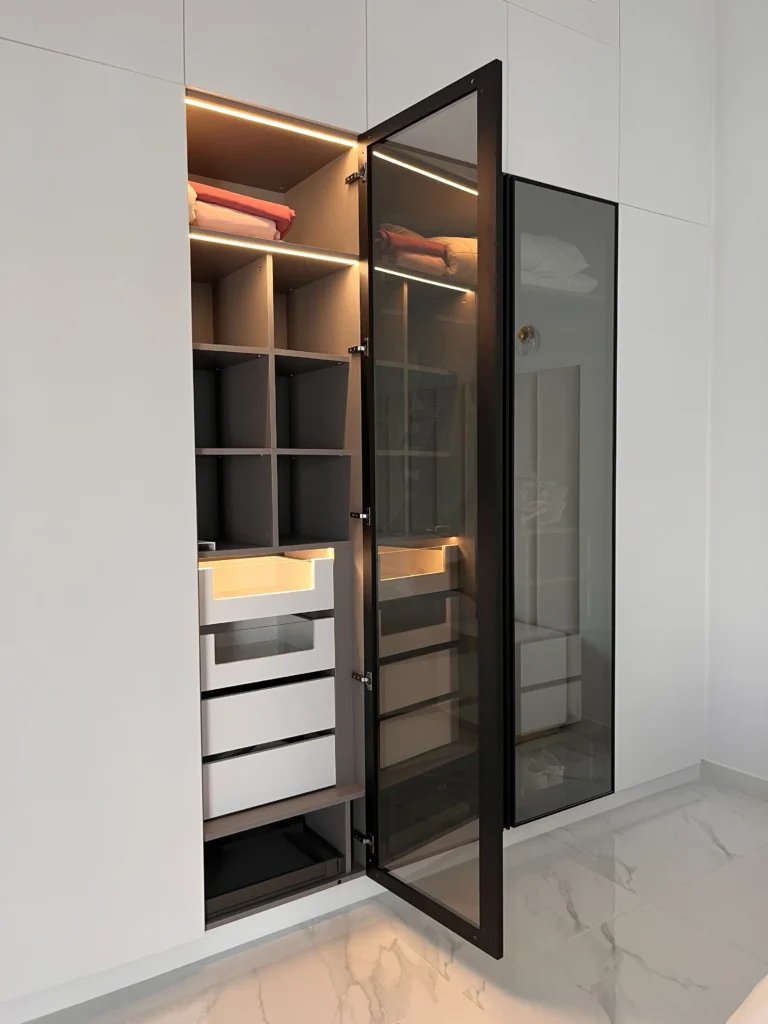 Contemporary wardrobe with glass doors, LED strip lighting, drawers, and shelving for neatly folded clothes.